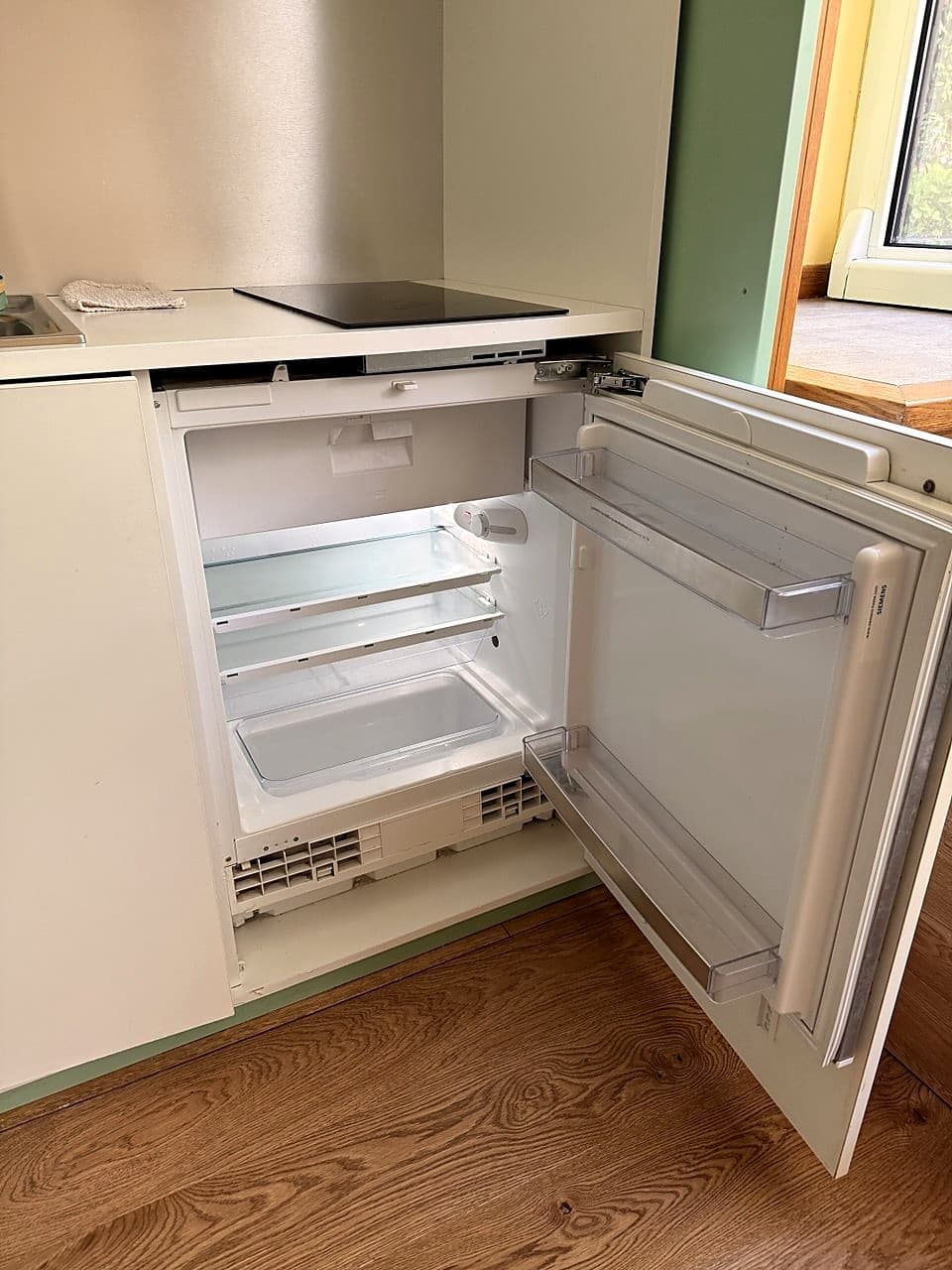 Frigorifero Siemens compatto incassato sotto il piano di cottura a induzione, aperto · due ripiani in vetro e cassetto in basso