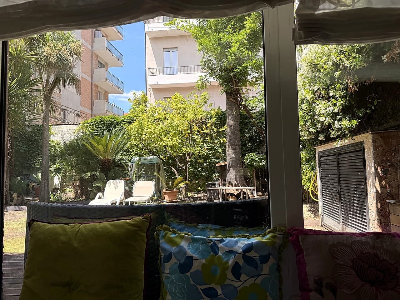 Vetrata a tutta parete che dà sul giardino, con cuscini floreali sul divano in primo piano